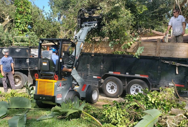GiANT G1200 loads branches into a trailer while two team members watch.