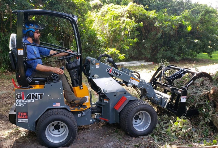 A man drives a G1200 TELE, loading sticks and branches into the grabber attachment